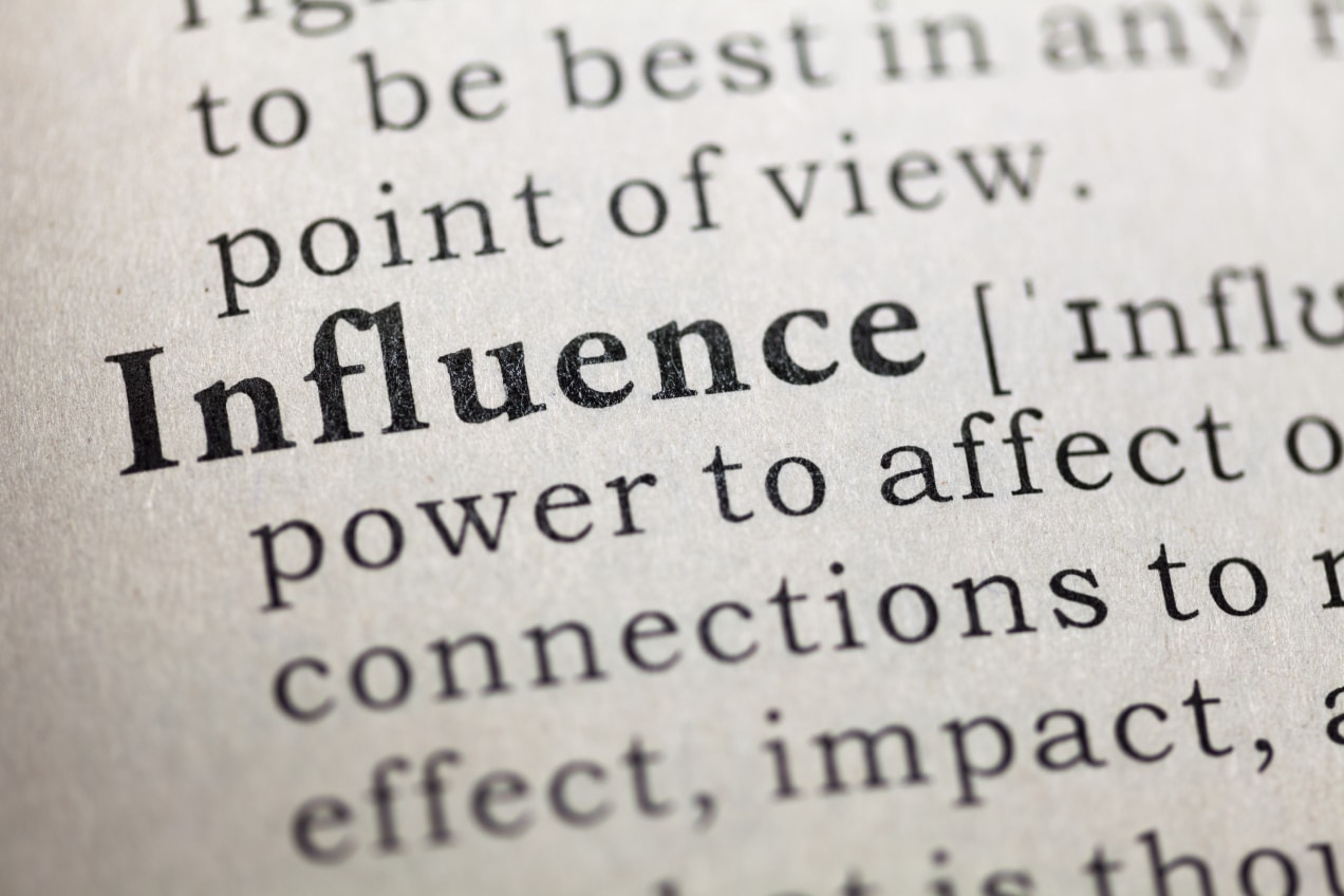 The image shows a close-up view of a dictionary page, focusing on the word "Influence." The definition is partially visible, stating that influence is the "power to affect or change something or someone." The text is in black print on a white background, with the word "Influence" highlighted in bold, drawing attention to its significance.