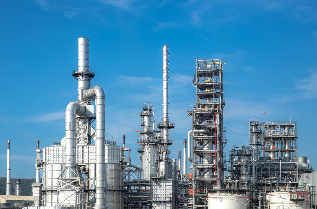 Industrial refinery complex with tall metal structures and pipelines under a clear blue sky, showcasing the scale and intricacy of modern industrial facilities.